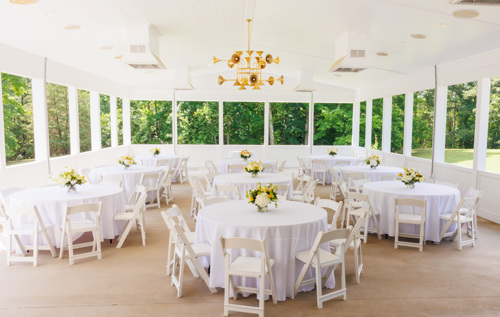 white wedding venue with gold chandelier and florals in peach, white, yellow and ivory table settings. White chairs, tables and linens. Open but covered outdoor wedding venue in Virginia winery