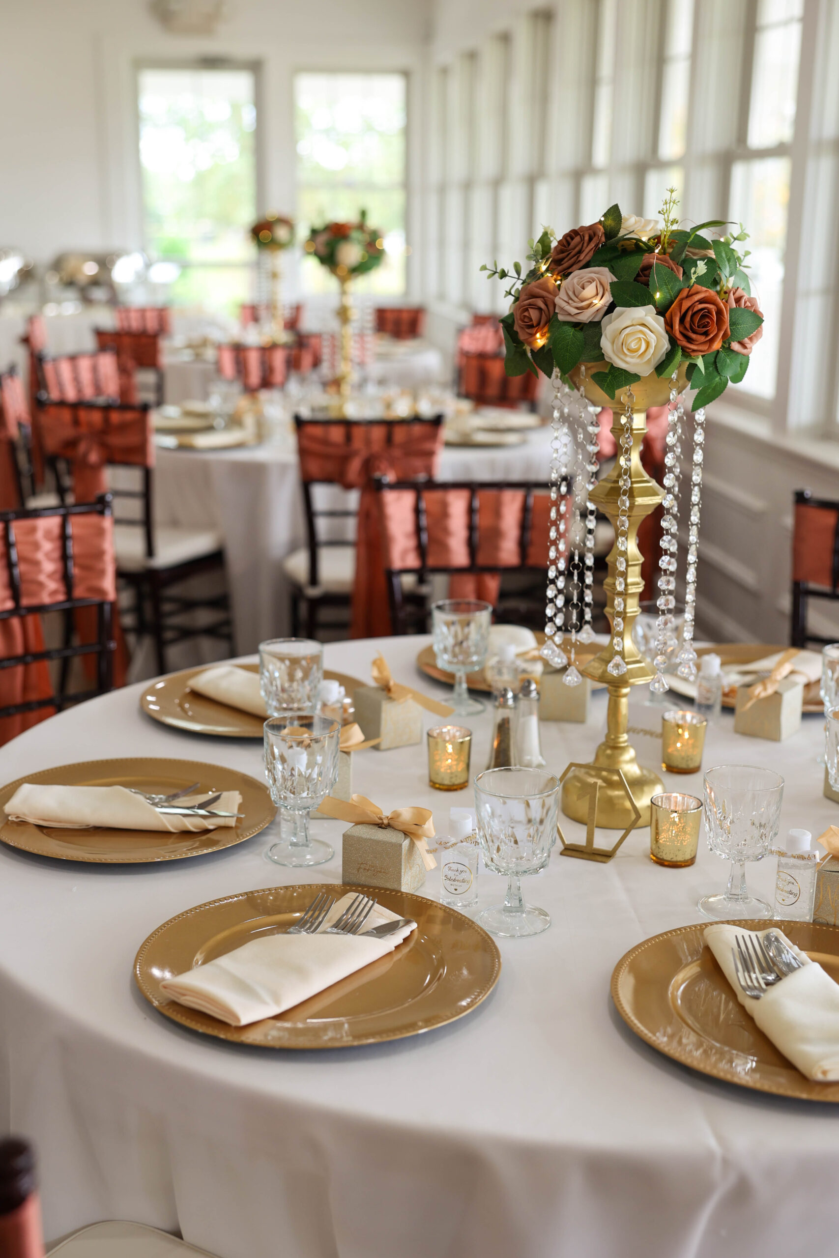 Wedding table settings in rose, gold, and ivory. Large topiary table centerpieces with flowers and pearls. Gold chargers for place settings.