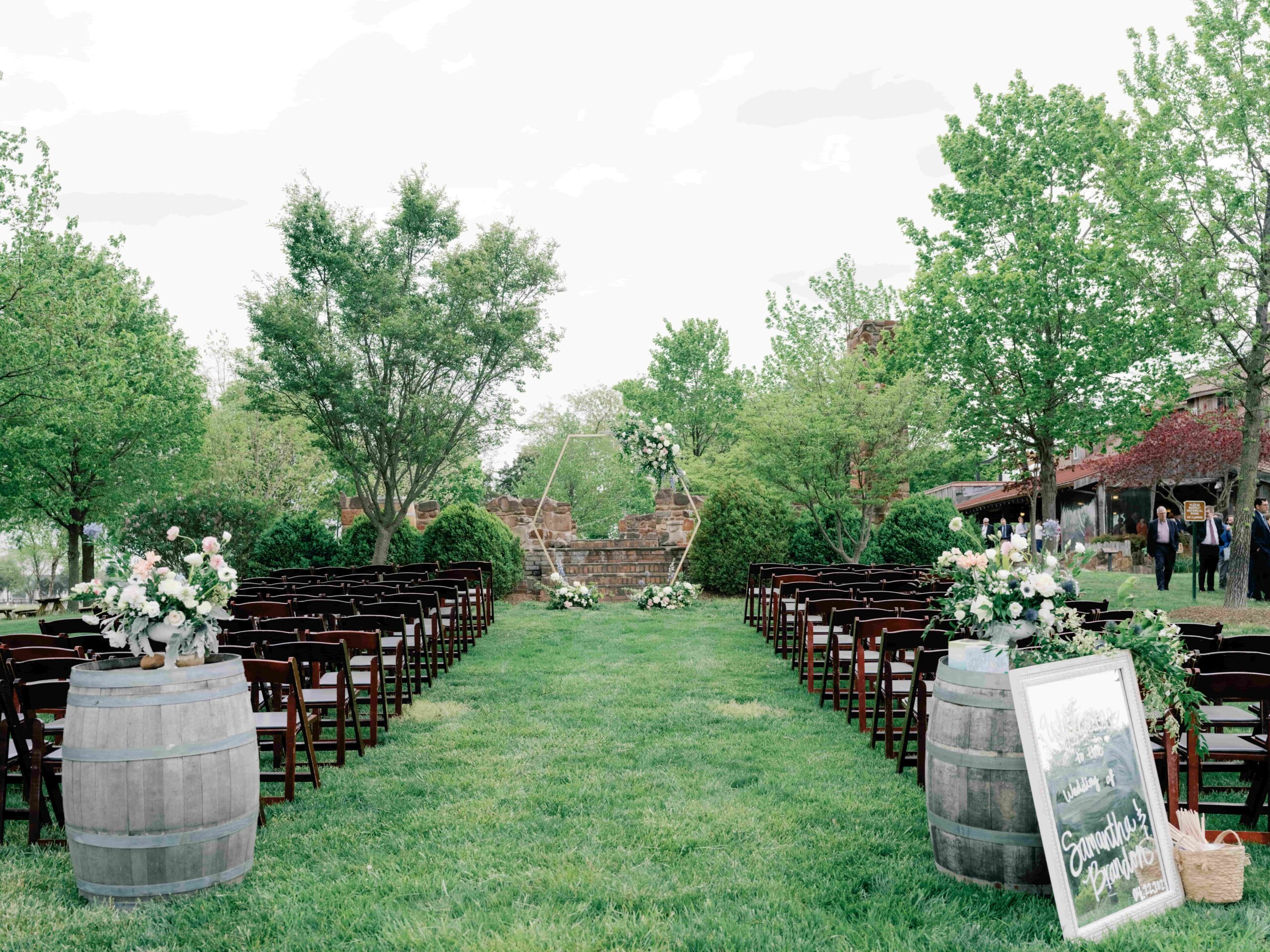 Rustic outdoor setting for a wedding at a winery. Rustic chairs, barrels on the bridal walk path with flowers on top.