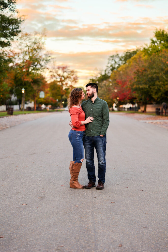 Couple in fall in Colonial Williamsburg before sunrise.  Standing embracing in a colonial street.  Changing fall leaves in the background.