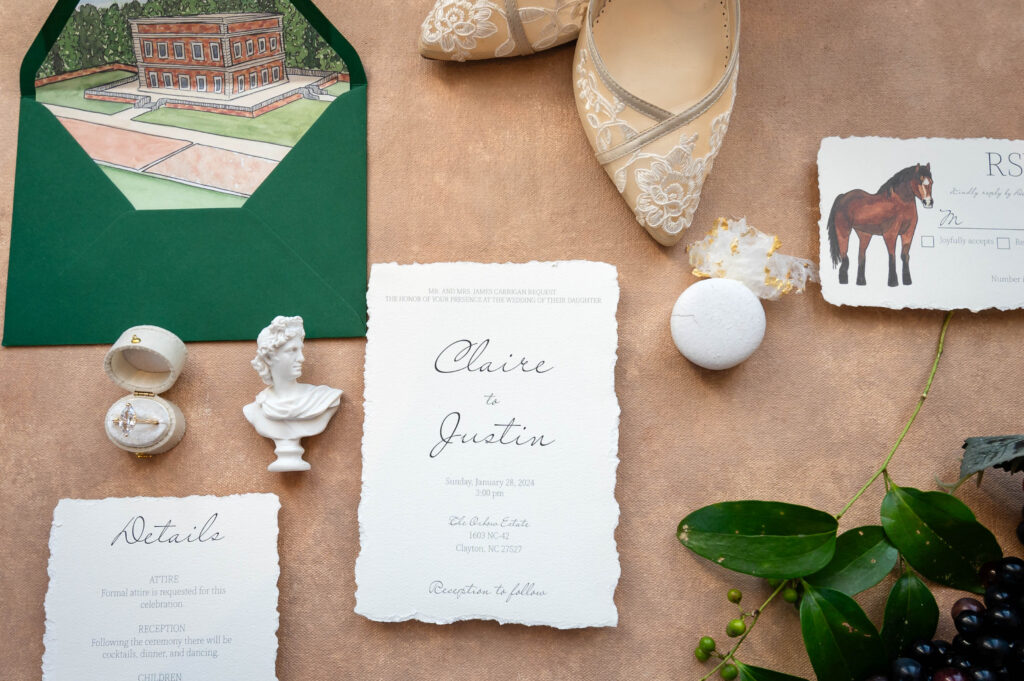 Flat lay of wedding day details of a wedding that included a horse.  In the flat lay are the invitation suite, Bride's lace wedding day shoes, her engagement ring and local greenery.  