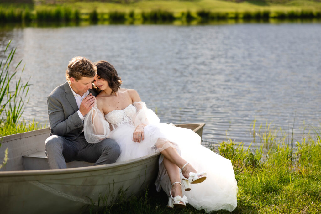 A bride and groom sitting in a boat by a peaceful lakeside, sharing an intimate and romantic moment on their wedding day.