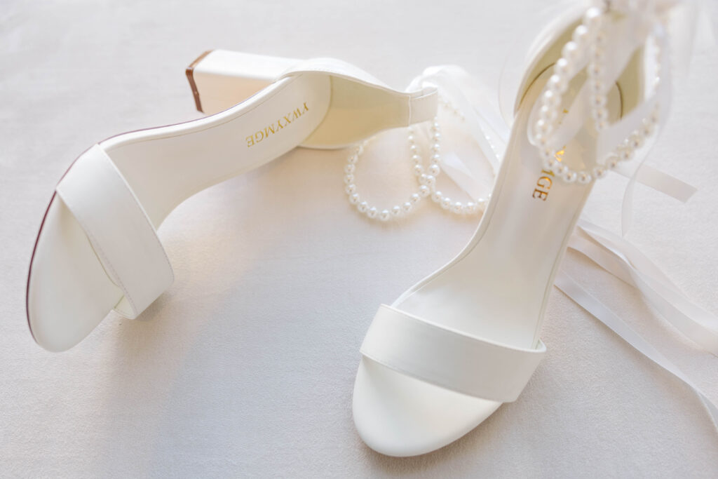 Elegant white bridal heels adorned with pearl accents, resting on a soft surface, ready for a wedding at The Marriott