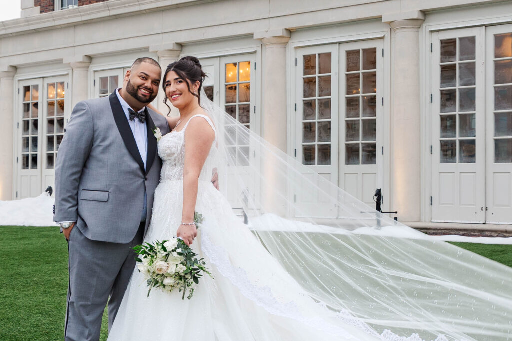 Bride and groom smiling together in front of the elegant exterior of The Virginia Cavalier, with the bride’s flowing veil and bouquet adding a romantic touch.